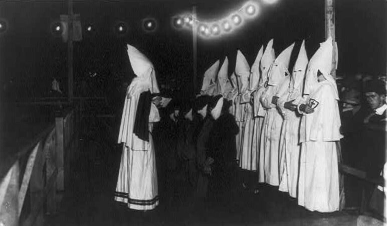 There is no known image of the WKKK in Monmouth County. This image shows the first public appearance of women of the KKK on Long Island. This photograph shows at least four women kneeling in front of shrouded Klansman reading from a book; other Klansmen stand behind them on the platform while spectators watch the initiation. Triangle Studio, photographer, created / published c1924. Library of Congress Prints and Photographs Division, Public Domain.